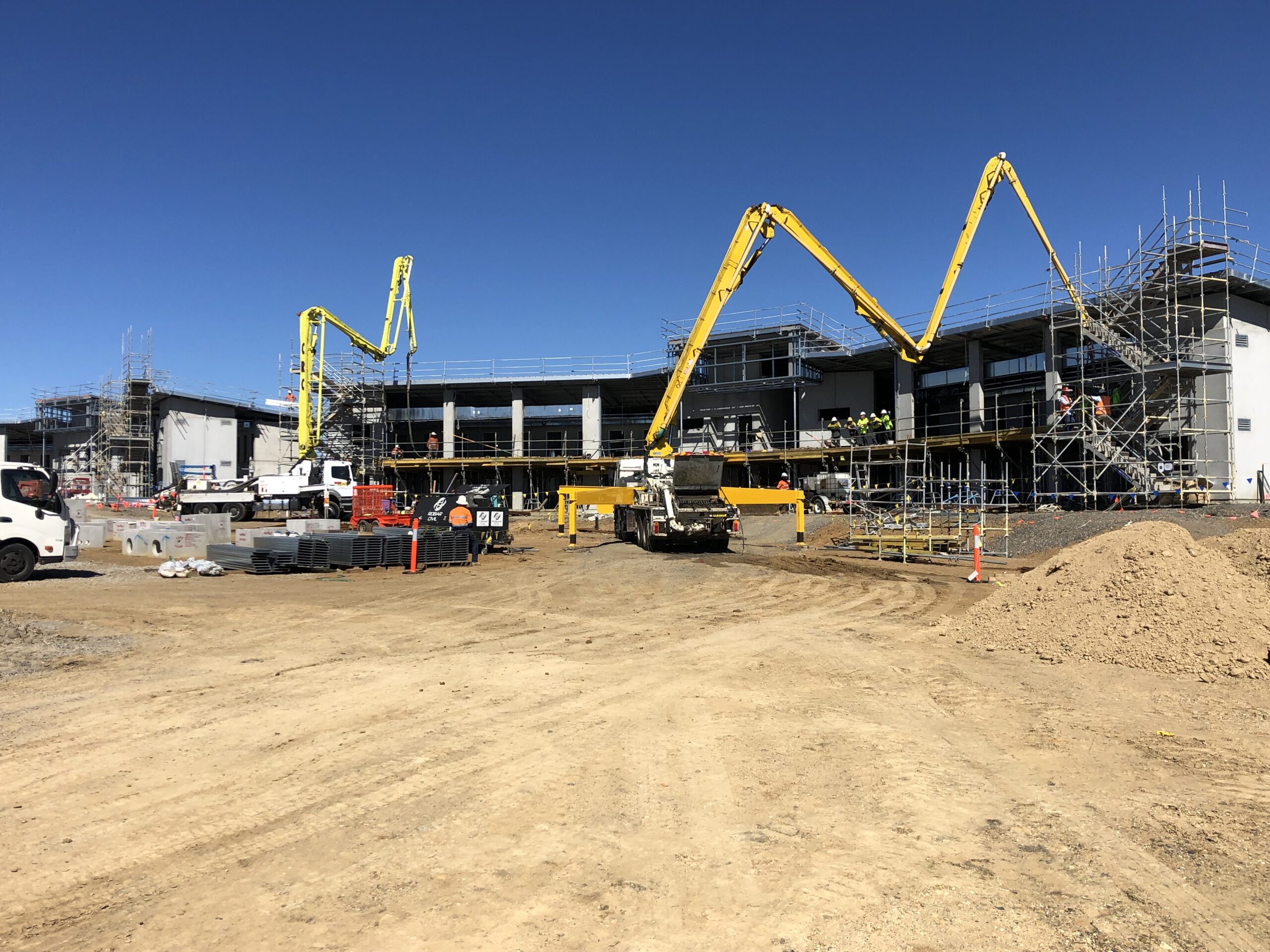 Three boom pump trucks operating together on a large-scale commercial building site under a clear blue sky in NSW